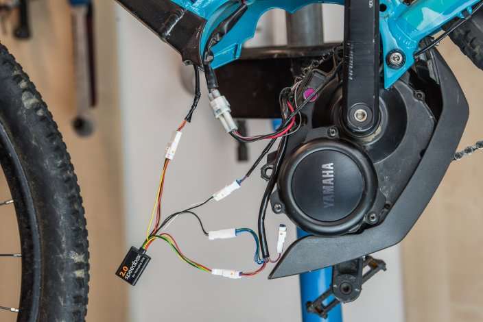 SpeedBox 2.0 module installed on Yamaha PW electric bike motor up to 2018, with wiring connectors visible on blue bike frame.